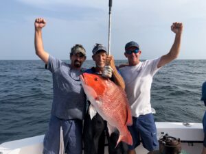 Three Men Smiling and Posing With an Orange Color Fish